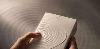 The Product Experience Begins Before the Package Opens Hands hold an unbranded textured package as ripples radiate from a fingertip.